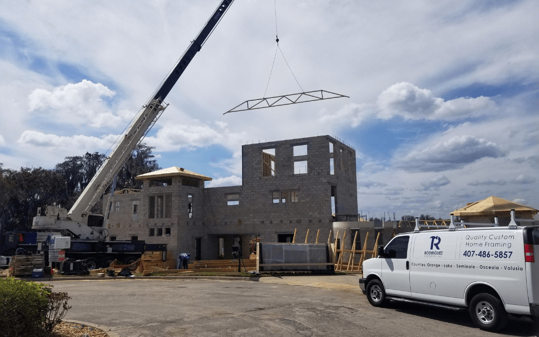 Construction crew using a crane to lift roof trusses on a custom home project in Clermont, FL, by Bridgethorn Construction, illustrating the building timeline.