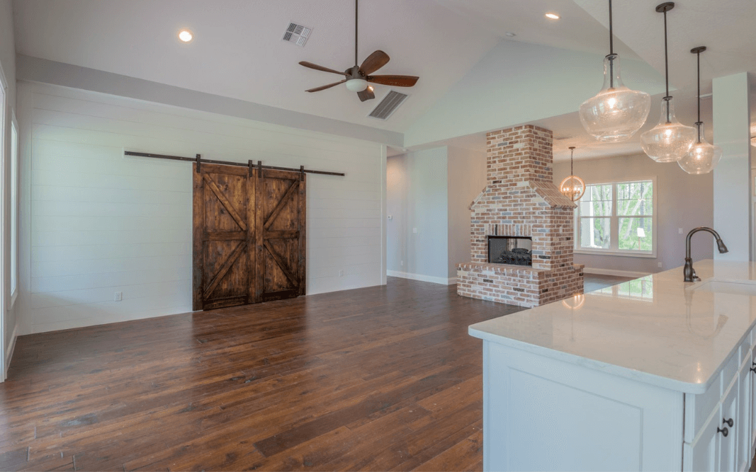 Spacious living room featuring a rustic barn door and brick fireplace, part of a custom farmhouse design in Clermont, FL.