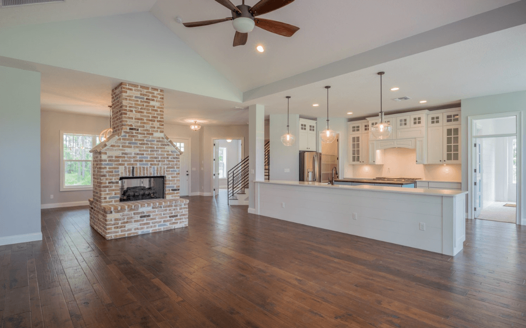 Open concept living area featuring a brick fireplace, white cabinetry, and pendant lights over a kitchen island in this Clermont, FL, custom home.